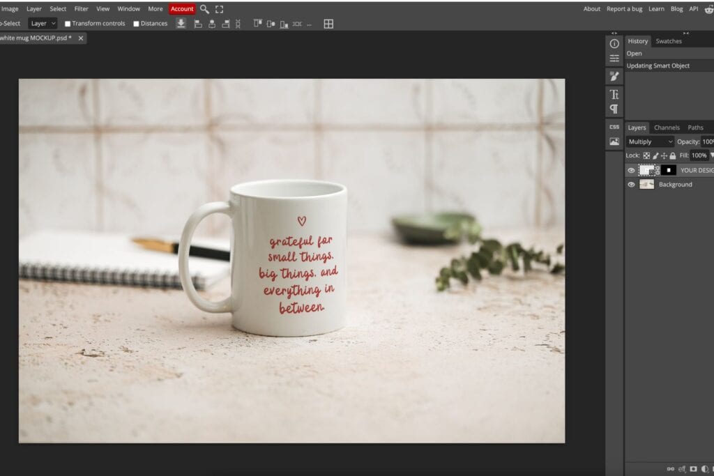 A photo editing software window displays a mug on a textured surface. The mug reads, grateful for small things, big things, and everything in between. There’s a notebook, a pen, and greenery in the blurred background.