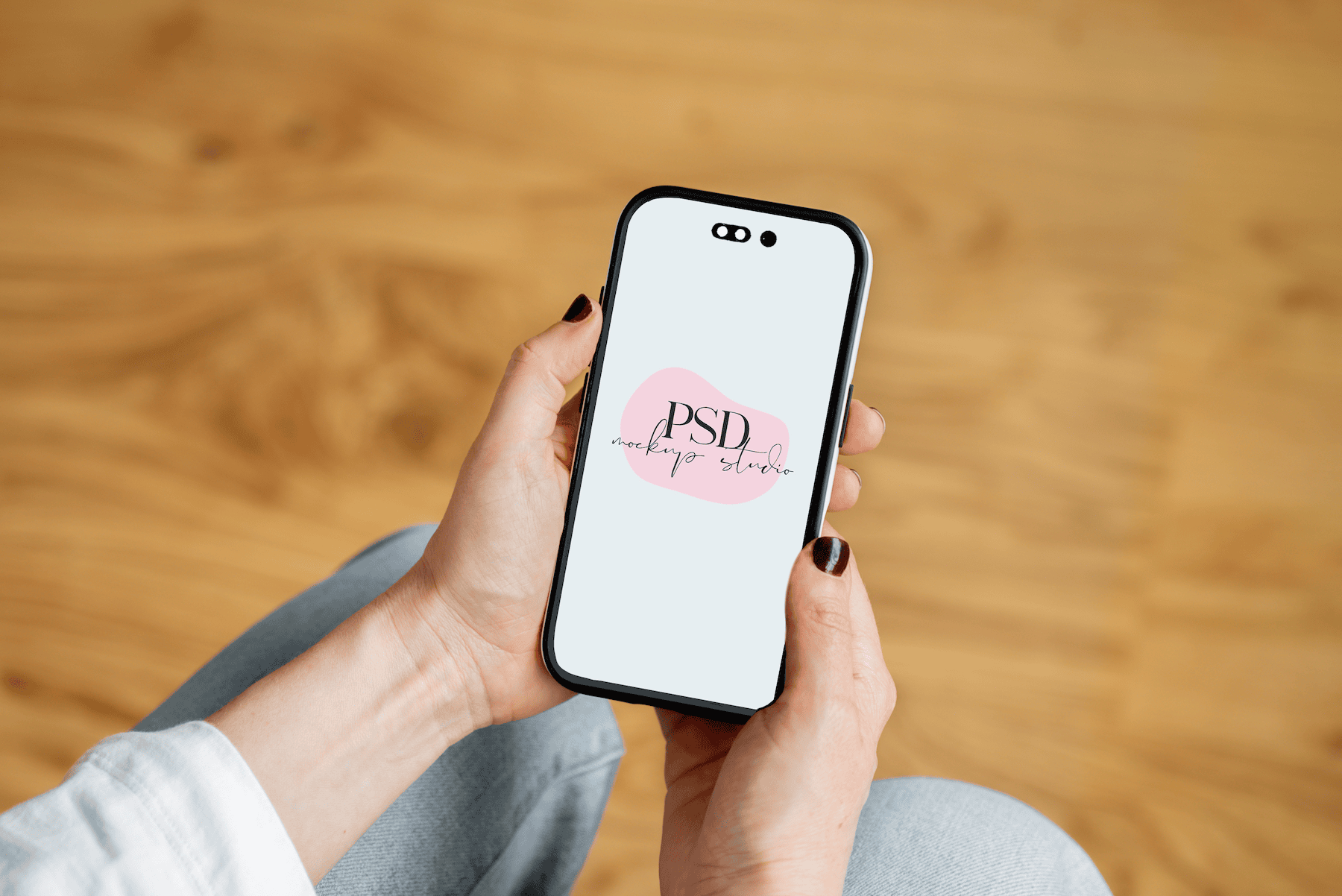 A person holds a smartphone displaying a logo that reads PSD mockup studio on a light background, with a blurred wooden floor in the background.